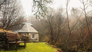 A stone cottage with a bench, surrounded by a grassy area and trees. - Find Me Out - Craigengillan Estate (Dalmellington)