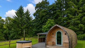 Eine Holzhütte mit gewölbtem Dach, einer kleinen Veranda und einem Whirlpool inmitten eines bewaldeten Gebietes.