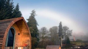 Eine Holzhütte mit Bogenöffnung, umgeben von Bäumen und einer nebligen Landschaft.