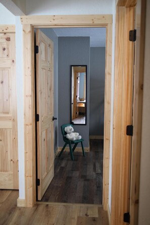 Un pasillo con puertas de madera, una silla verde y un espejo en la pared.