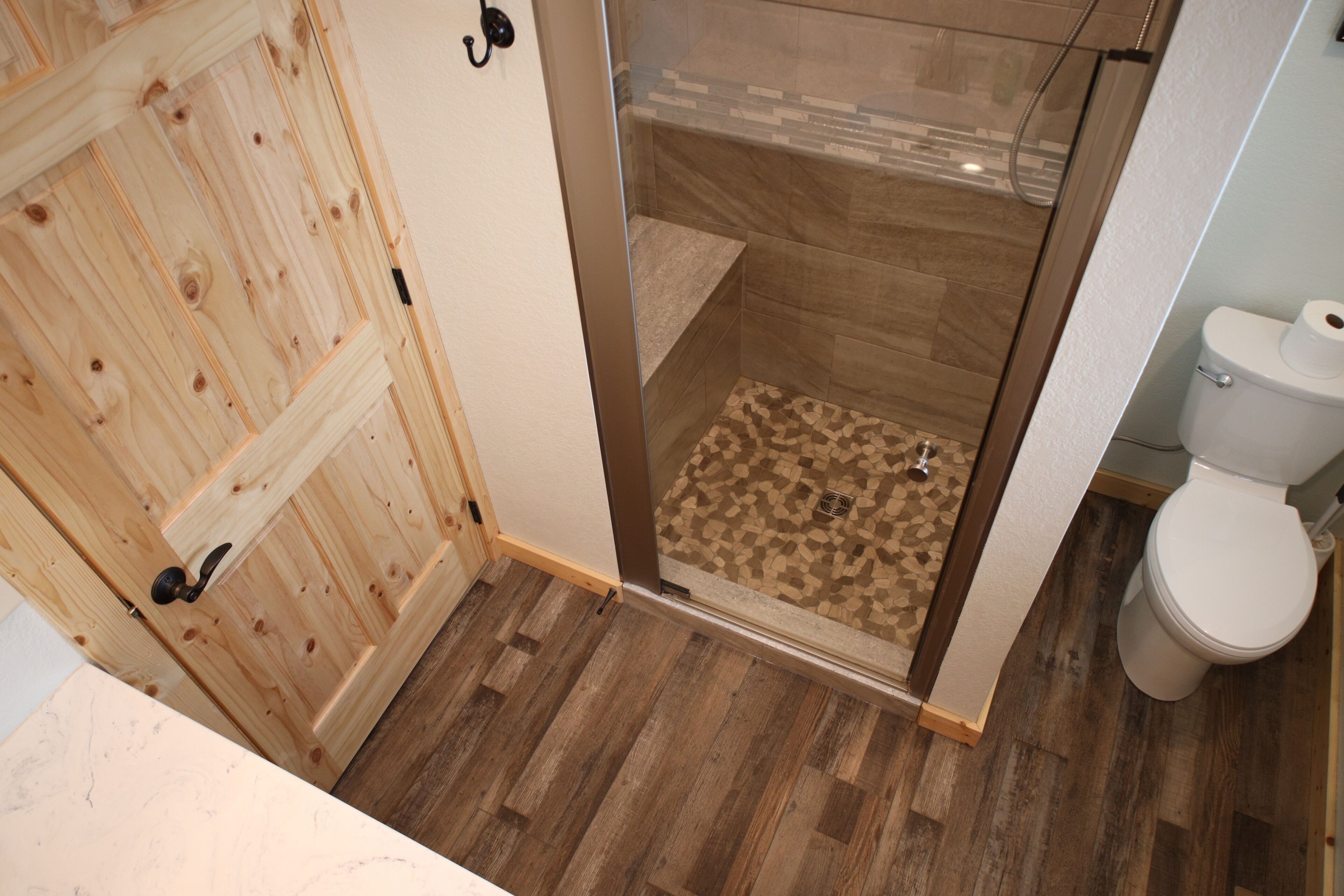 En trædør, et brusebad med mosaikfliser og et toilet.