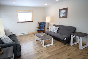 Una sala de estar con un sofá gris, una mesa de centro de madera, un sillón azul y una lámpara.