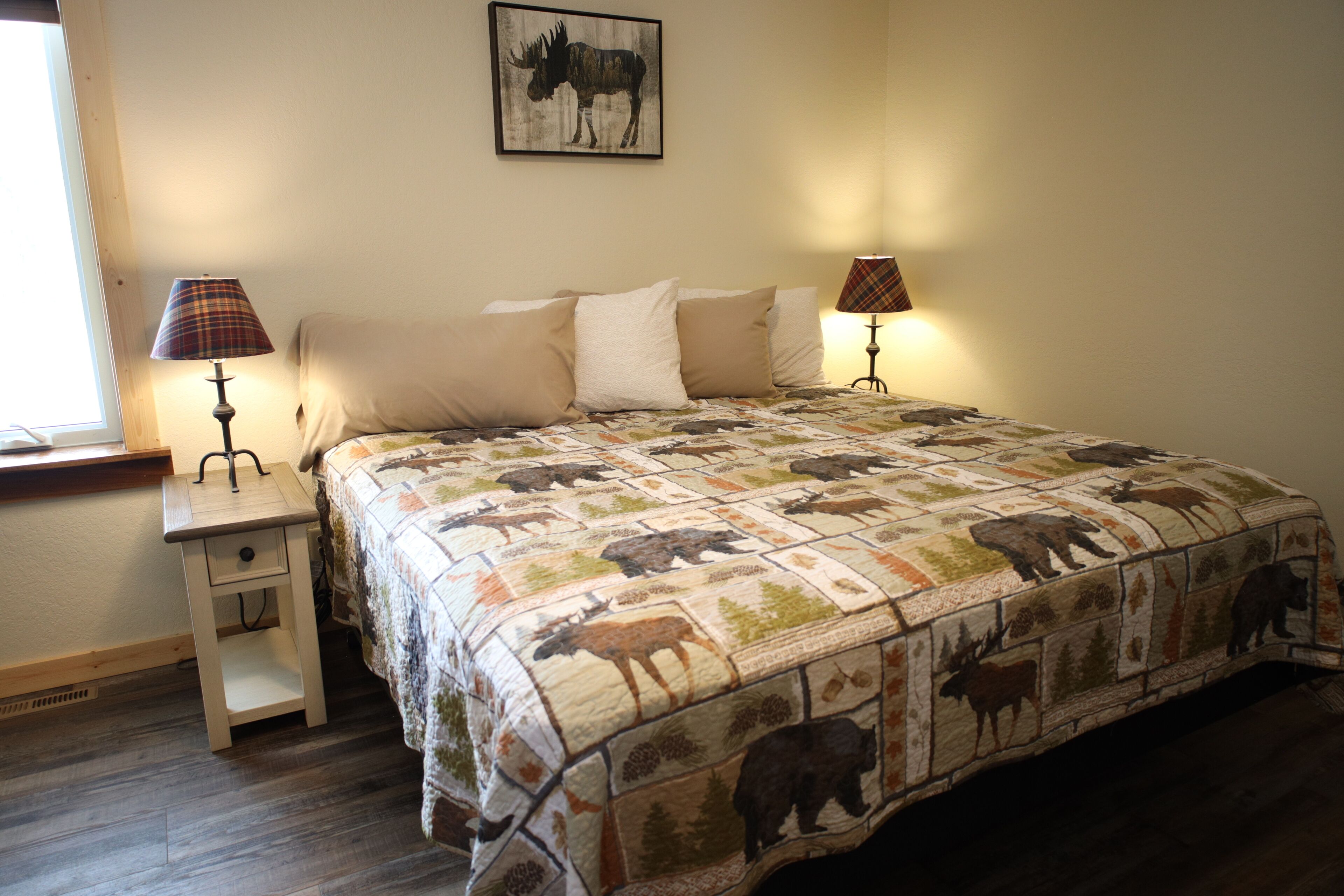 A bedroom with a bed, two bedside lamps, a nightstand, a window, and a wall-mounted picture.