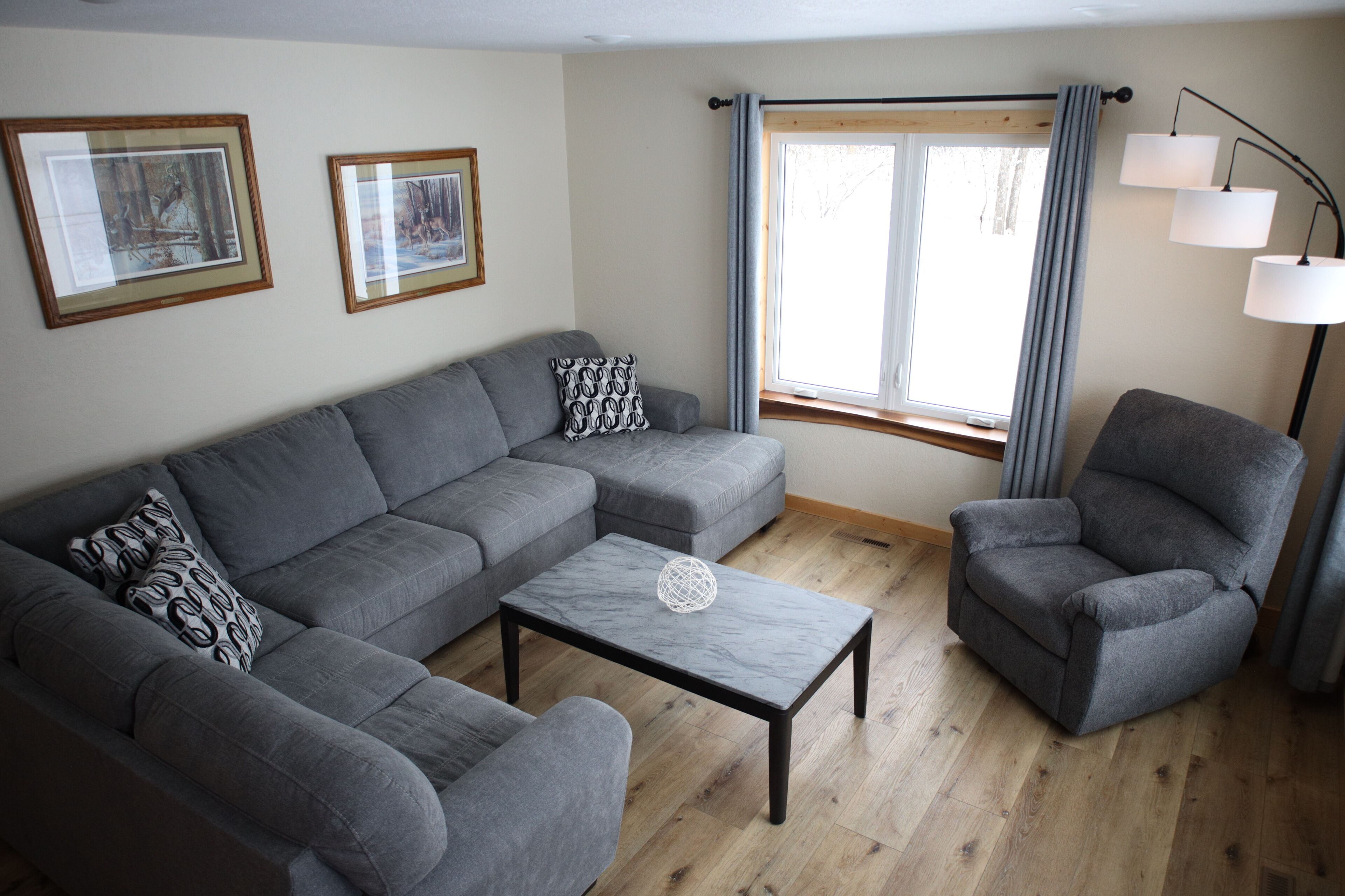 A living room with a grey sofa, a matching armchair, a marble coffee table, and a floor lamp.