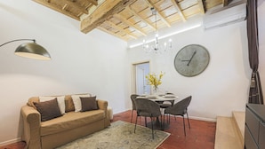 A living room with a sofa, a chandelier, a dining table with chairs, and a clock on the wall. - Apartments Florence - Mezzo Boutique Vista (Firenze)
