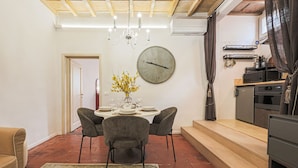 A dining area with a round table, chairs, a clock, and a vase with flowers. - Apartments Florence - Mezzo Boutique Vista (Firenze)