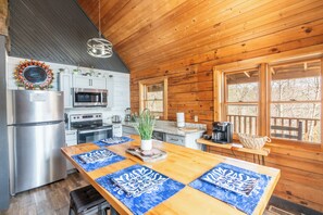 A wooden cabin kitchen with a refrigerator, microwave, stove, and wooden dining table with blue placemats. - Treetopia Ridge - A Rare Find among 1 Bedroom Cabins - Master Suite +Children's Loft +Guest Quarters (Sevierville)