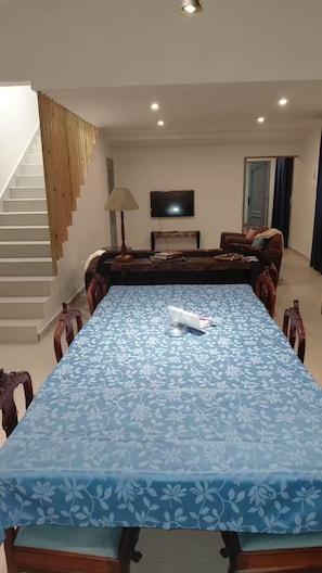 Un espace repas comprenant une longue table, des chaises, un escalier, un téléviseur et une porte.