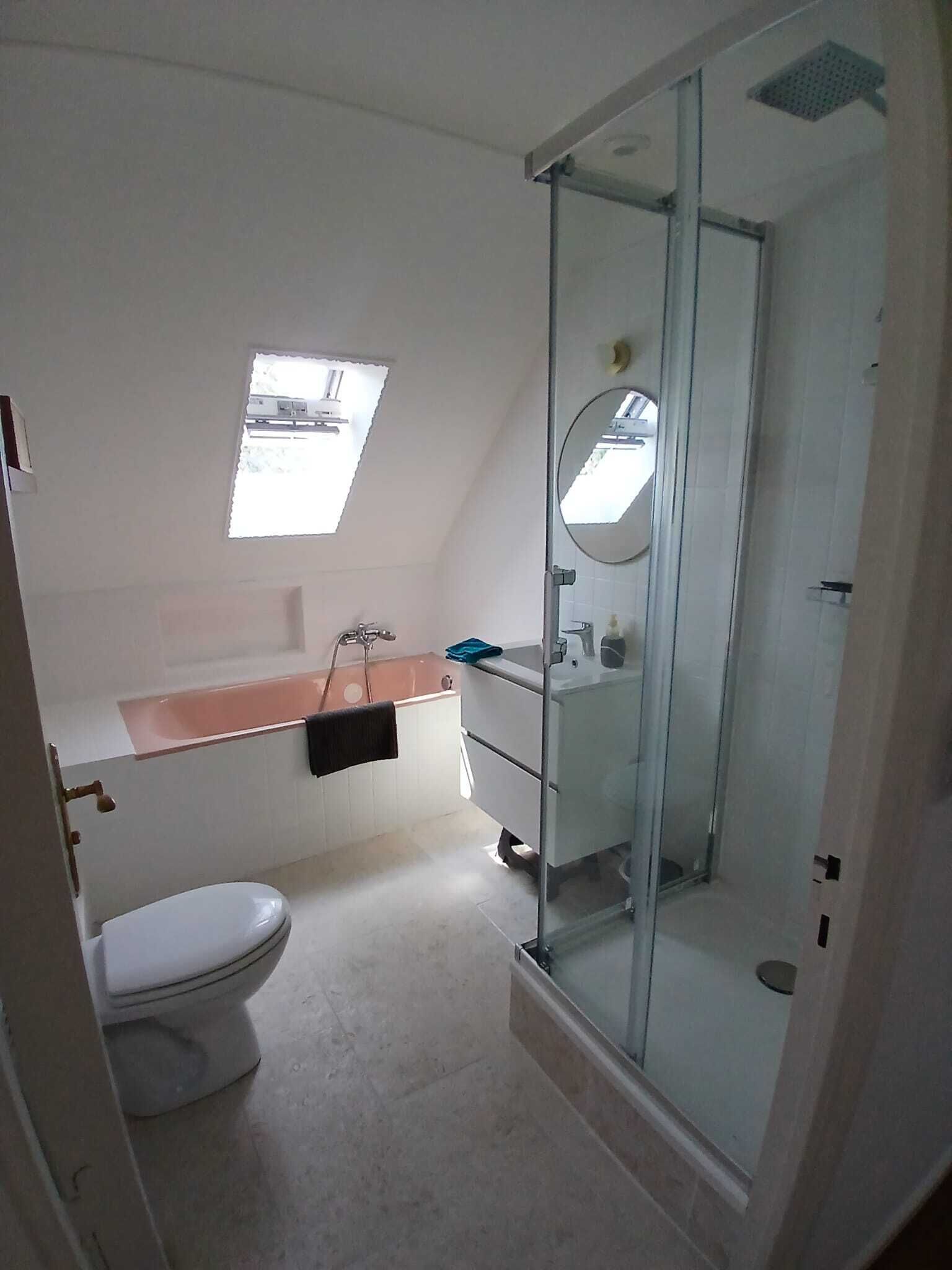 A bathroom with a toilet, a glass-enclosed shower, a sink with a mirror, and a small window.
