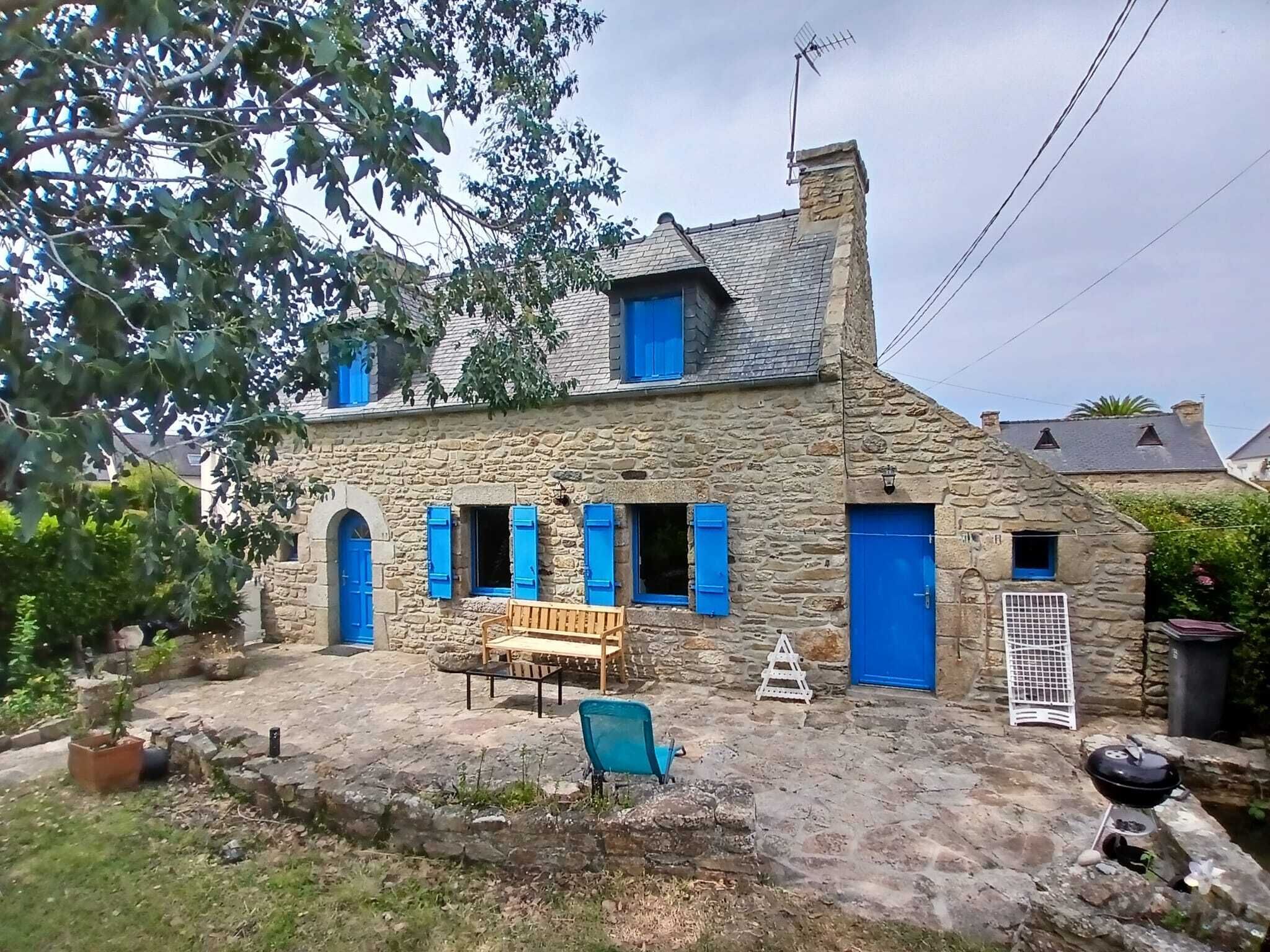 A stone house with a chimney, a wooden bench, and a barbecue grill in the yard.