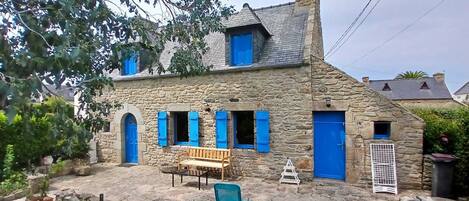 Une maison en pierre avec une cheminée, un banc en bois et un barbecue dans la cour.