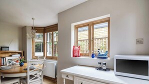 Una cocina con microondas, armarios de madera, una mesa de comedor con sillas y una ventana que ofrece vistas a edificios.