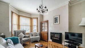 Una sala de estar con chimenea, televisor, candelabro y un ventanal con persianas.
