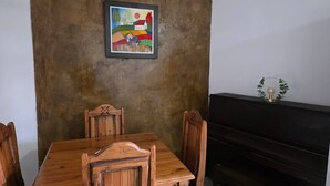 Uma sala de jantar com uma mesa e cadeiras de madeira, um quadro na parede e um piano.