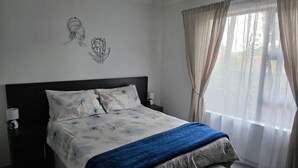 Quarto com cama, mesas de cabeceira, uma janela com cortinas e decoração na parede.