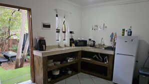 Cozinha compacta com pia embutida, micro-ondas e geladeira. Há uma pequena janela com cortinas, e vista para um jardim lá fora.