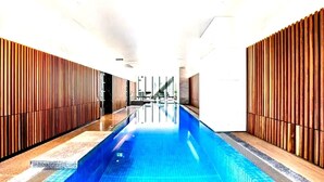 A swimming pool with a tiled deck, flanked by wooden panel walls, and a staircase in the background. - BNBIFY Stylish Melbourne CBD 2BR Apartment | Pool, Spa, Gym (Melbourne)