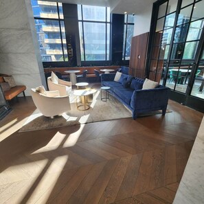 A spacious lounge area with a blue sofa, white armchairs, and a coffee table. Large windows provide natural light and views of the city. - BNBIFY Stylish Melbourne CBD 2BR Apartment | Pool, Spa, Gym (Melbourne)