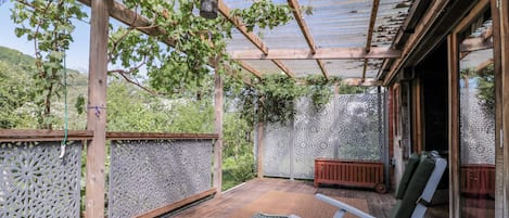 A covered outdoor seating area with a pergola, wooden benches, and a table with a bottle and glasses.