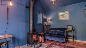 Una habitación con una estufa de leña, un sofá azul, un tapete estampado, una mesa de madera y un espejo en la pared.