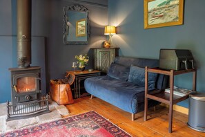A cozy room with a wood-burning stove, a sofa, a table with a lamp, and a framed painting on the wall. - Ferryman's Lodge (Chepstow)