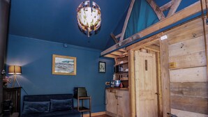 Una habitación acogedora con pared azul, techo de madera, un sofá, una alfombra y una puerta que da a otra habitación.