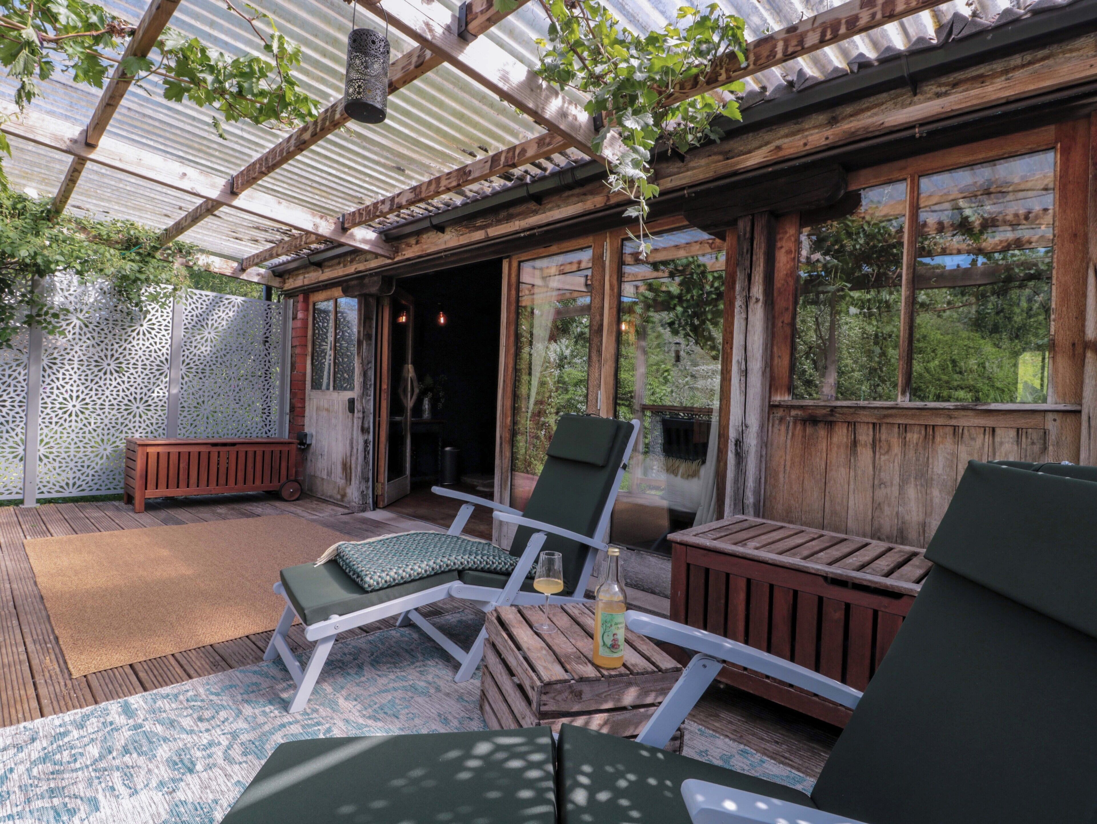 Une terrasse extérieure aménagée avec du mobilier en bois, une pergola et une vue sur la verdure environnante.