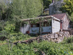 Ein rustikales Steinhaus mit Holzveranda, umgeben von üppiger Vegetation und Bäumen.