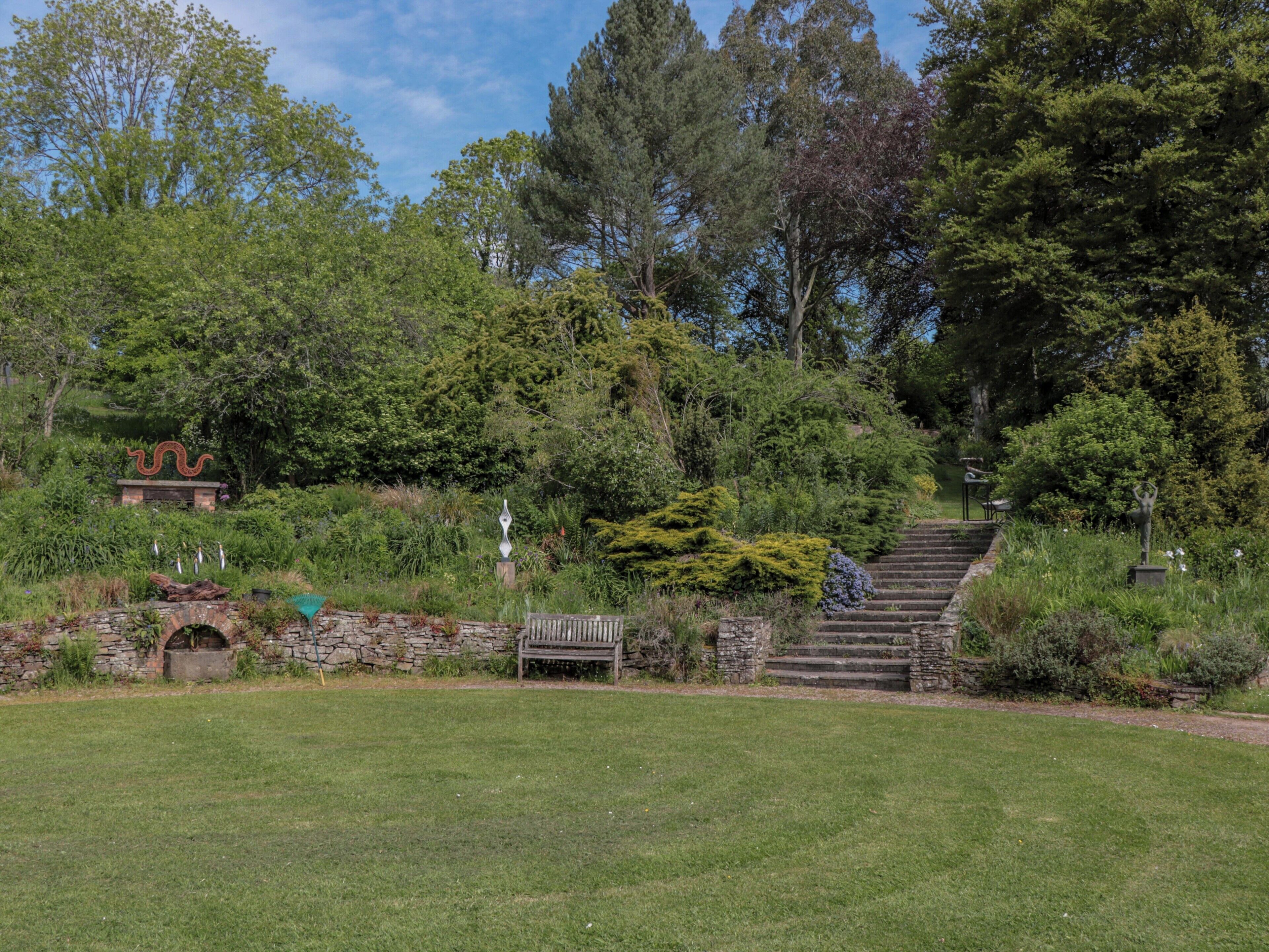 Un jardin agrémenté d’un escalier en pierre, d’un banc en bois et d’une statue.