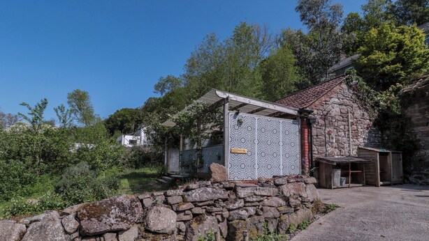 Un muro de piedra, una valla metálica con diseño y un edificio con techo de tejas.