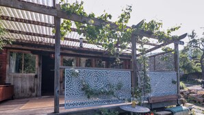 Una terraza de madera con un pérgola, un enrejado blanco decorativo y una pequeña mesa redonda con un banco.