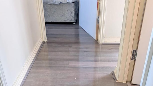A hallway with wooden flooring leading to a bedroom with a bed and a nightstand. - 3 bed House Upto 6 Adults (Tilbury)