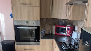 A kitchen with wooden cabinets, a stainless steel oven, a microwave, a red toaster, and a gas stove. - 3 bed House Upto 6 Adults (Tilbury)