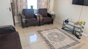 A living room with two armchairs, a coffee table, a TV, and a decorative rug. - 3 bed House Upto 6 Adults (Tilbury)