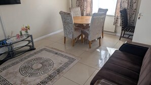 A living room with a brown sofa, a dining table with chairs, a coffee table, and a decorative rug. - 3 bed House Upto 6 Adults (Tilbury)