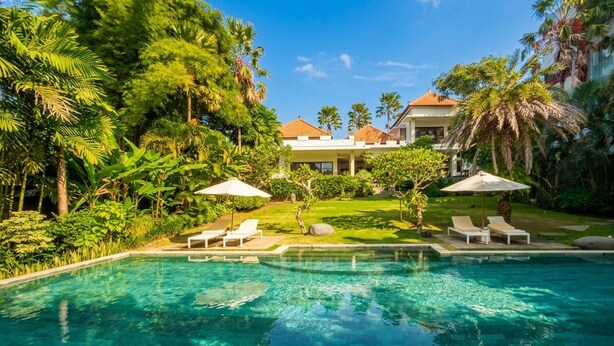 Une piscine entourée d’une végétation luxuriante et un bâtiment doté d’un toit en tuiles.