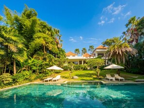 A pool surrounded by lush greenery and a building with a tiled roof. - Villa Athaya Pererenan by Beranda (Canggu)