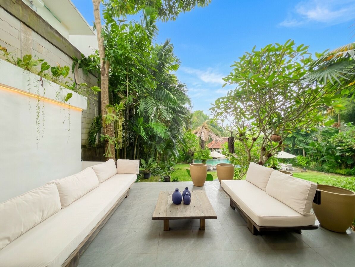 A patio with two beige sofas, a wooden table with two vases, and large planters.
