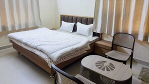 Un dormitorio con cama, mesita de noche, silla y una pequeña mesa redonda.
