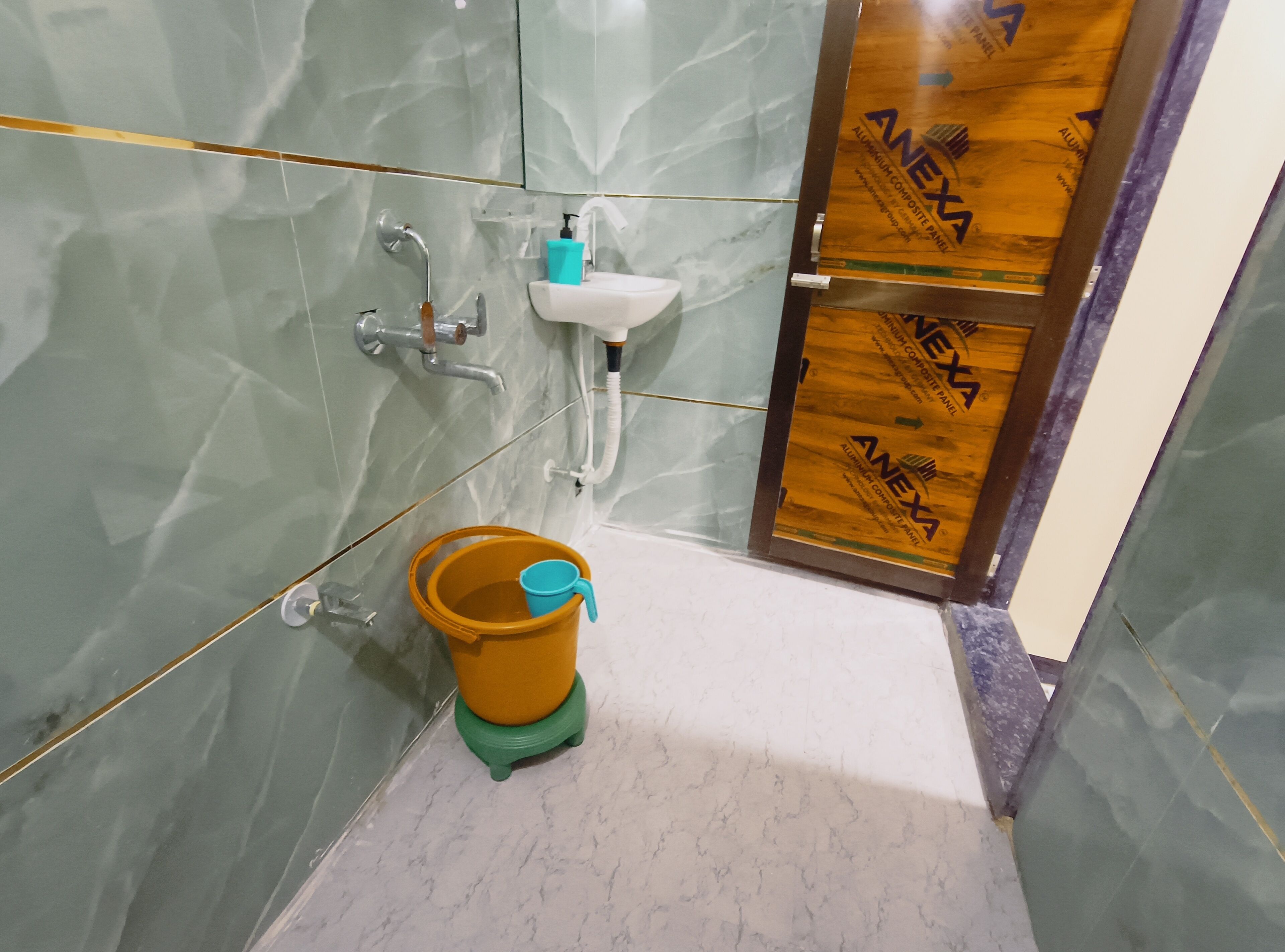 A bathroom with a marble wall, a sink, a shower, and a wooden door.
