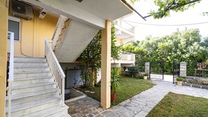 Ein Wohngebäude mit einer Treppe, die zu einem Zwischenpodest führt, einem gepflasterten Weg und einem gepflegten Garten mit einer Umzäunung.