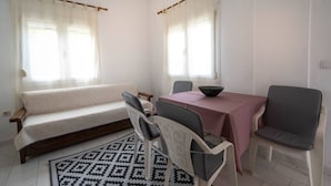 A room with a sofa, a dining table with chairs, a patterned rug, and a window with curtains. - Erato Apartment 1 by RentalsPro - Nea Plagia Halkidiki (Plagia)