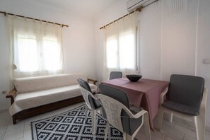 Ein Zimmer mit einer Couch, einem Esstisch mit Stühlen, einem gemusterten Teppich und einem Fenster mit Vorhängen.
