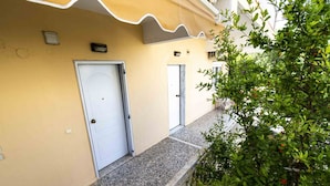 A building with two white doors, a balcony with a railing, and a small table. - Erato Apartment 1 by RentalsPro - Nea Plagia Halkidiki (Plagia)