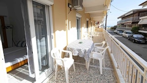 A balcony with a table and chairs, a sliding glass door, and a view of parked cars and buildings. - Erato Apartment 1 by RentalsPro - Nea Plagia Halkidiki (Plagia)