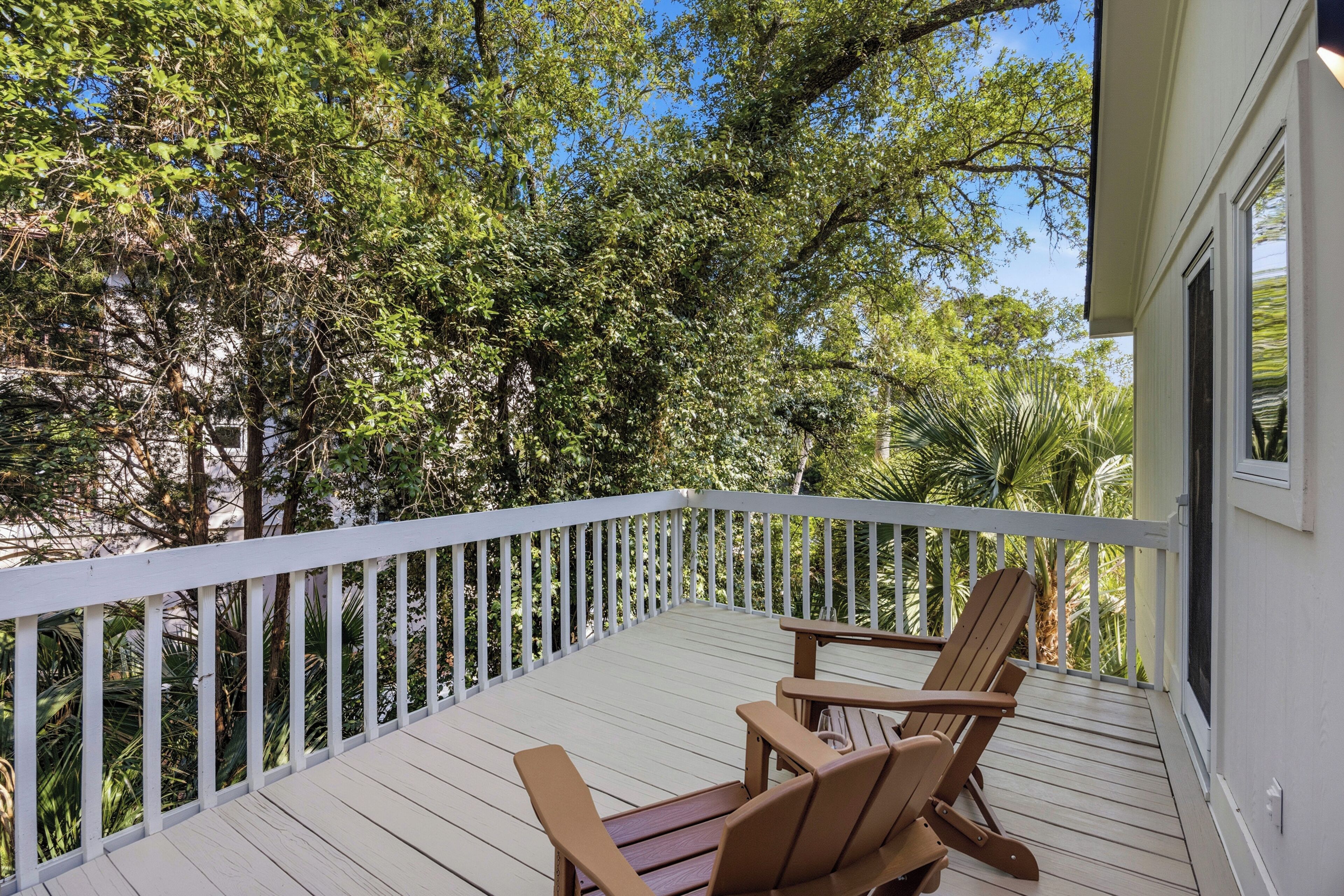 Une terrasse en bois avec une balustrade blanche, deux chaises en bois et une vue sur des arbres et un bâtiment.