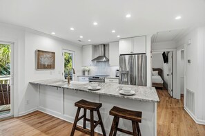 Une cuisine moderne dotée d’un îlot en marbre, d’appareils électroménagers en acier inoxydable et de tabourets de bar en bois.