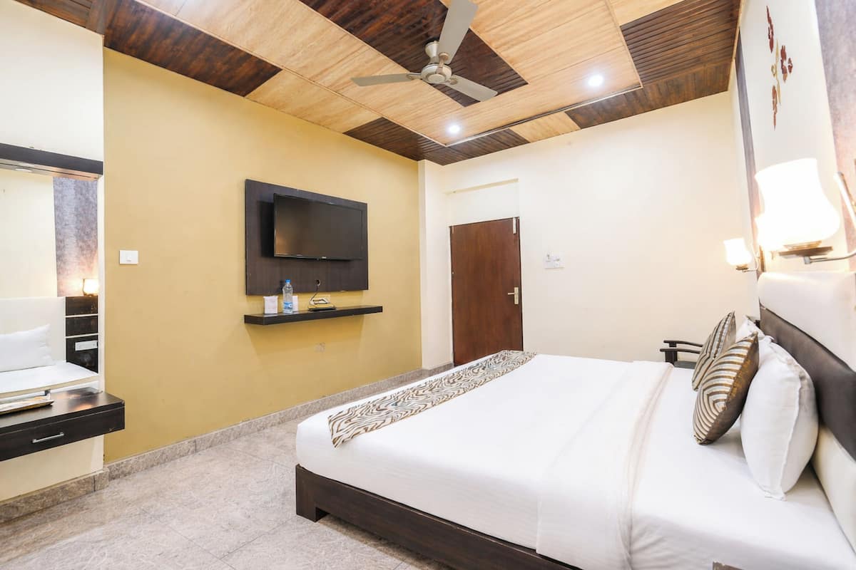 Una habitación de hotel con una cama, un televisor montado en la pared, un ventilador de techo y una puerta.