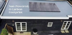 Un edificio moderno con techo solar, fachada oscura y un pequeño jardín.