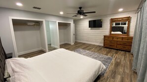 Quarto com cama, cômoda, ventoinha no teto, televisão e closets espaçosos.